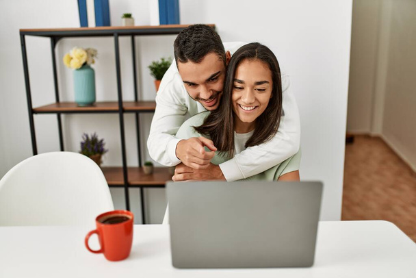 Jeune couple latin utilisant ordinateur portable et boire du café à la maison. - Photo, image