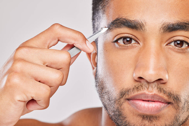 On my way to perfect eyebrows. Shot of a young man plucking his eyebrows against a grey background. - Foto, afbeelding