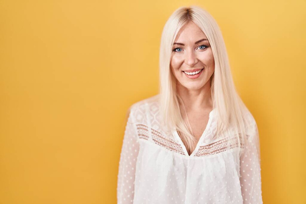 Caucasian woman standing over yellow background looking positive and happy standing and smiling with a confident smile showing teeth  - Foto, imagen
