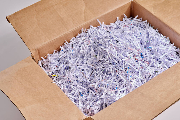 Shredded paper is great for packing. Studio shot of shredded paper in a cardboard box against a grey background. - Foto, imagen