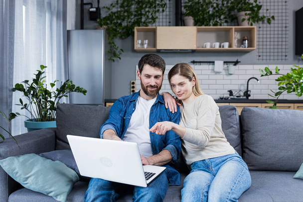 Online shopping. Family, man and woman at home, sitting on the couch, buying goods online from a laptop, holding a credit card in their hands. Happy, smiling, hugging - Φωτογραφία, εικόνα