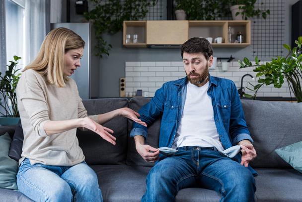 A young woman demands money from her husband, the man does not show empty pockets. At home, sitting on the couch. Quarrels, conflicts, misunderstandings. Money crisis - Foto, Bild