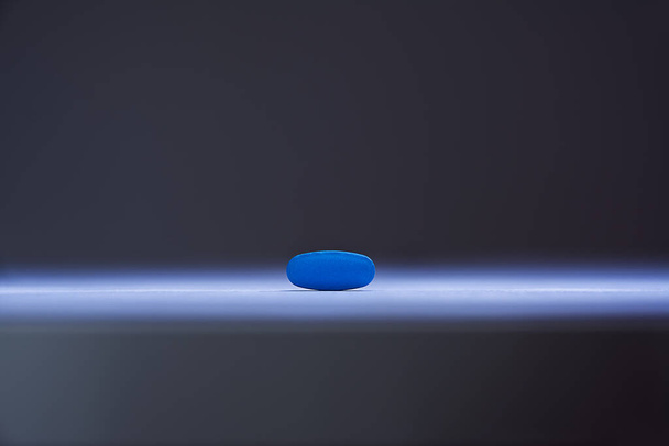Eine einzige blaue Pille beleuchtet durch einen einzigen scharfen Strahl - Foto, Bild