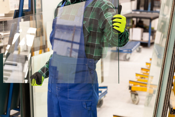 Der Glaser trägt eine Glasscheibe in der Hand, die Glasfabrik  - Foto, Bild