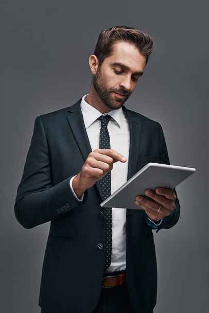 Legato al mondo aziendale. Studio foto di un bel giovane uomo d'affari che utilizza un tablet digitale su uno sfondo grigio. - Foto, immagini