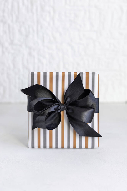 Caja de regalo envuelta en papel geométrico rayado con lazo de cinta negra de cerca. Navidad, Año Nuevo, Cumpleaños, Concepto de aniversario - Foto, imagen