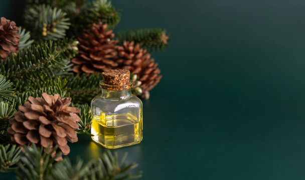 Glass bottle with conifer essential oil near fir branches and pine cones on green close up. Aromatherapy, spa and herbal medicine concept. Natural remedy or cosmetics. - Fotoğraf, Görsel