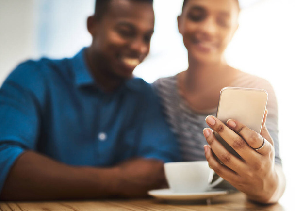 Het leren kennen van je deel van de date. Schot van een jonge man en vrouw die samen een mobiele telefoon gebruiken op een date in een coffeeshop. - Foto, afbeelding