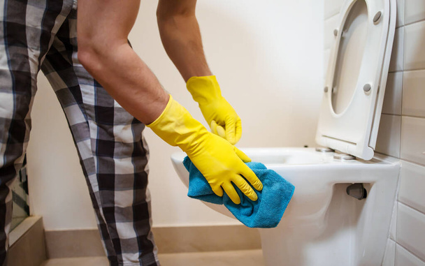 man wearing gloves clean the toilet with a sponge in the bathroom - Foto, immagini