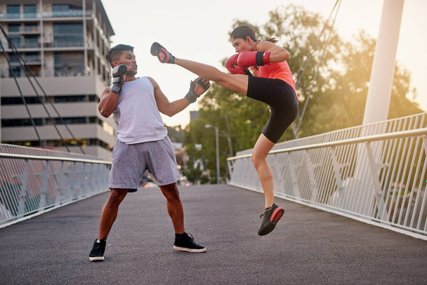 Elle bosse sur ses coups de pied. Prise de vue d'un jeune couple passant par des routines de kickboxing à l'extérieur sur un pont. - Photo, image