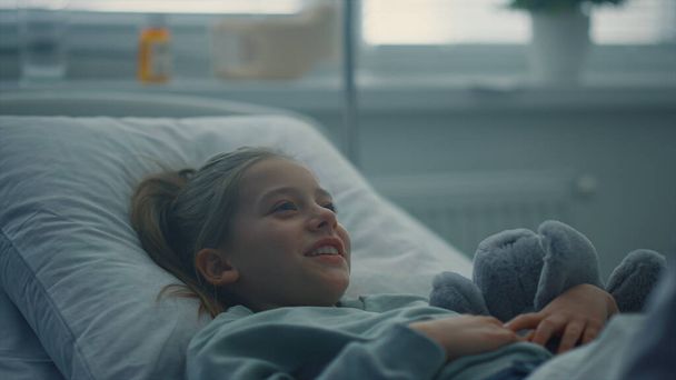 Portrétní dívka ležící na nemocničním lůžku objímající hračku. Lékař na návštěvě pacienta v oddělení. - Fotografie, Obrázek