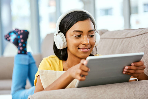 I have such a variety of music I can choose from. Shot of a teenage girl listening to music and using a tablet at home. - Foto, afbeelding