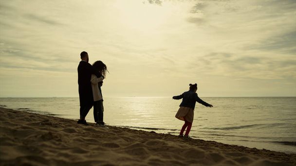 Родители ребенка расслабляются вместе на пляже каникулы. Семья веселится на берегу моря - Фото, изображение
