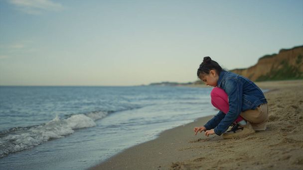 Cute girl gra piasek na plaży morskiej. Dzieciak cieszący się wakacjami na wybrzeżu przyrody. - Zdjęcie, obraz