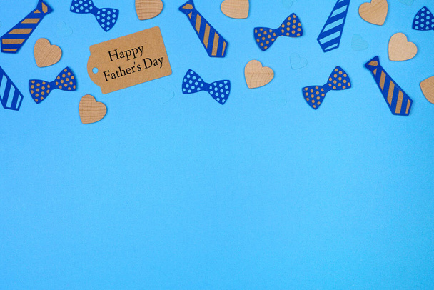 Étiquette cadeau Happy Fathers Day avec bordure supérieure des décorations de cravates en papier et des cœurs en bois sur un fond en papier bleu. Vue aérienne avec espace de copie. - Photo, image
