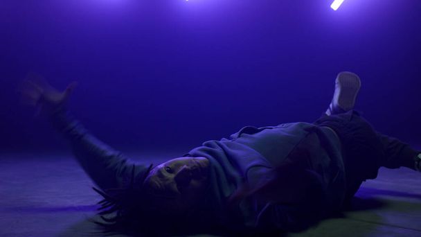Stylish breakdancer moving body lying dance floor in club ultraviolet lights. - Фото, зображення