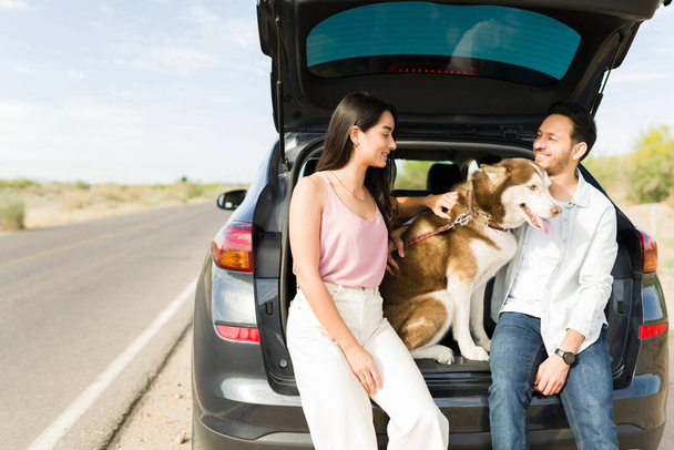 Attractive hispanic couple petting their dog and resting from driving from a holiday vacation  - Zdjęcie, obraz