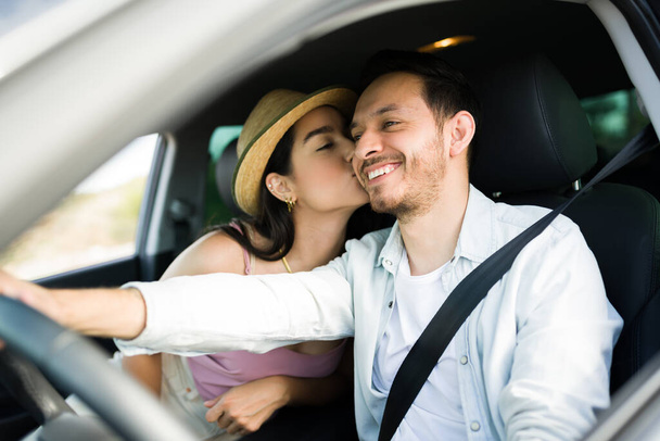 Attractive young woman giving a kiss on the cheek to her boyfriend while driving together for vacations - Фото, изображение