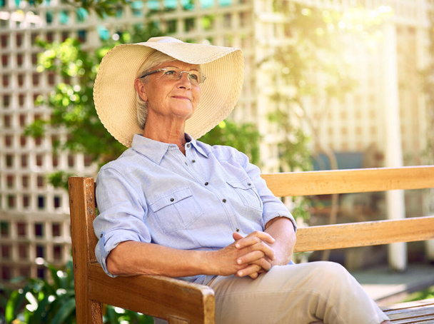 Уход на пенсию, время для отдыха и размышлений. Снимок заботливой пожилой женщины, отдыхающей на скамейке в саду. - Фото, изображение