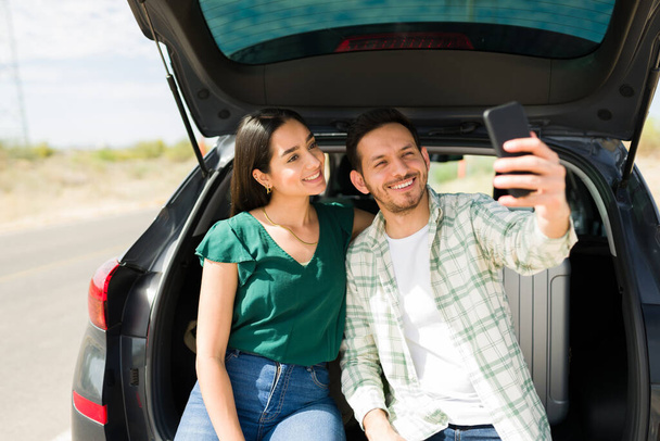 Cheerful hispanic couple taking a selfie for social media while taking a road trip together  - Foto, Imagen
