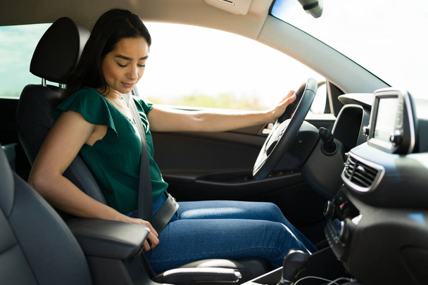 Naispuolinen nuori kuljettaja laittaa turvavyönsä päälle noustessaan autoon aloittaakseen ratsastusjakosovelluksen.  - Valokuva, kuva