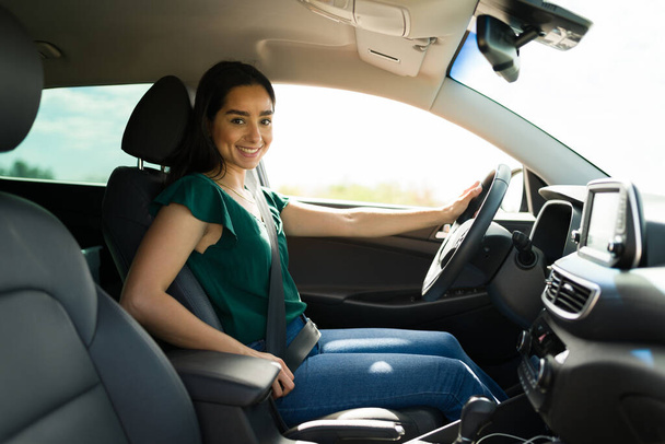 Portrait of a beautiful latin woman putting on the safety seat belt and smiling behind the wheel - 写真・画像