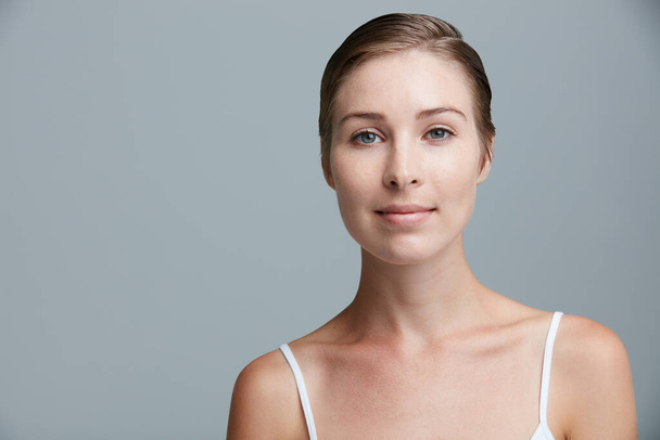 Minder make-up, meer mij. Studio portret van een aantrekkelijke jonge vrouw poseren tegen een grijze achtergrond. - Foto, afbeelding