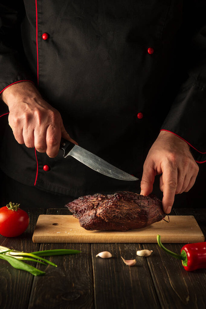 The chef cuts the baked beef steak with a knife on a wooden table. The concept of the cooking process. - Foto, Imagem