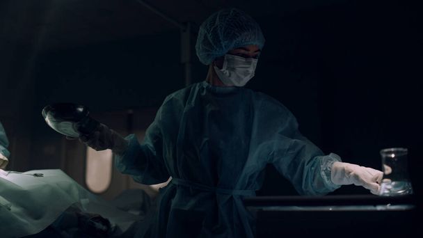 Professioneller Chirurg, der in der dunklen Notaufnahme operiert. Zusammenarbeit im medizinischen Team - Foto, Bild