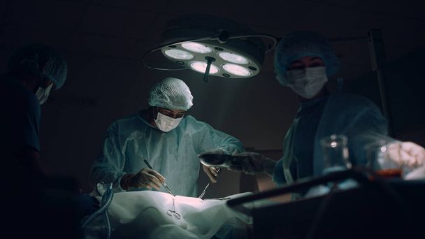 Zespół lekarzy wykonujący operacje chirurgiczne na sali operacyjnej ciemnego szpitala. - Zdjęcie, obraz