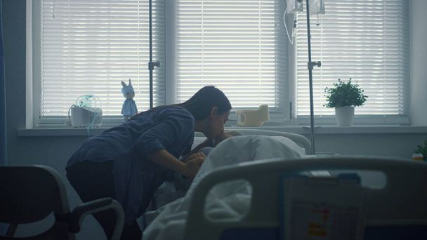 Mother kissing sick daughter lying in bed. Supportive parent visit patient ward - Photo, Image