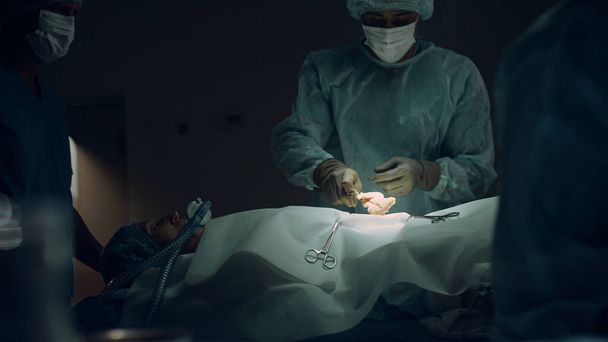 Pielęgniarka zajmująca się sterylnymi instrumentami zbliżenie ciemni. Współpraca zespołu medycznego - Zdjęcie, obraz