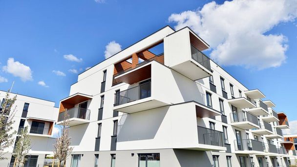 Teil eines weißen Wohnhauses mit Balkonen und blauem Himmel mit Wolken. Architektonische Details in einem modernen Mehrfamilienhaus an einem sonnigen Tag. - Foto, Bild