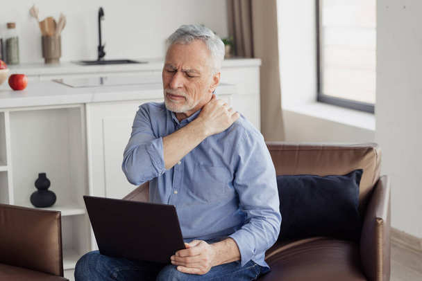 Trpící starší muž cítí bolest ramene nebo krku po práci na notebooku. Důchodce s chronickým zraněním, zánětem, masáže unavené svaly a potřebují lékařskou péči nebo zdravotní péči - Fotografie, Obrázek