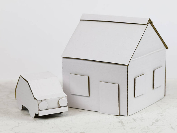 Будинок моделі разом з моделлю автомобіля поруч зроблені з білого картону. Разом ці два пункти символізують майно, сімейний будинок або іпотеку, або інші значення нерухомості.
. - Фото, зображення