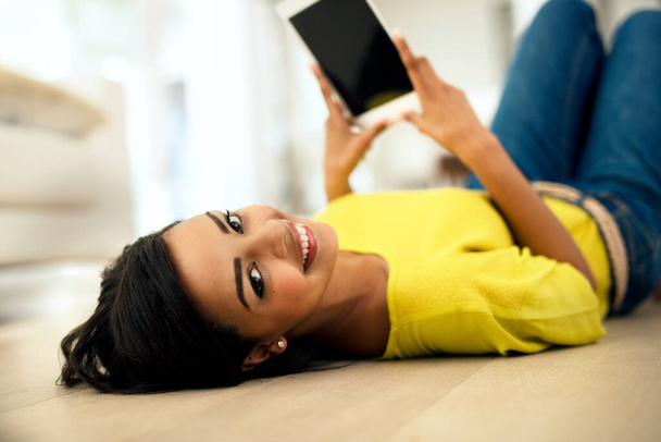 My new tablets great. Shot of a young woman using a digital tablet while lying on the floor at home. - Valokuva, kuva