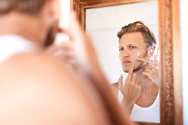Just when I thought I was pimple-free. Shot of a young man examining his skin in the mirror at home. - Φωτογραφία, εικόνα