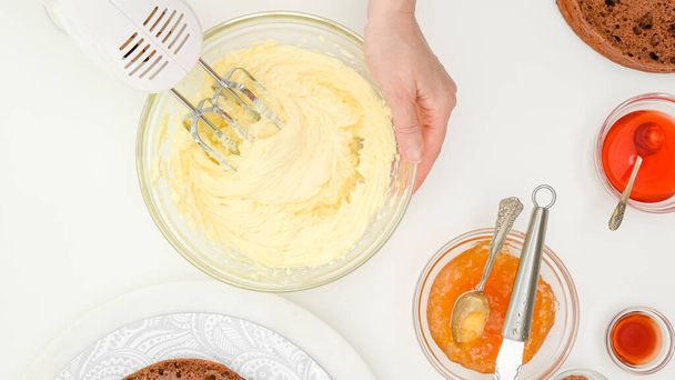 Butter cream, jam, syrup close up in bowls. Woman hands mixing cream using an electric mixer. Step by step chocolate cake recipe. Ingredients close up on kitchen table, flat lay - Foto, Bild