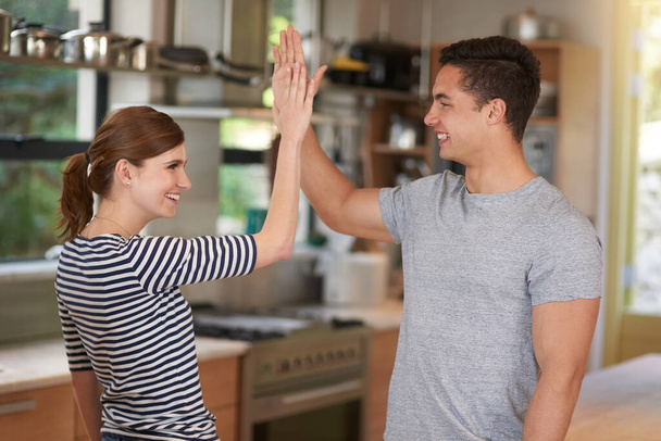 Great job baby. Shot of a happy young couple high-fiving in their kitchen at home. - Фото, изображение