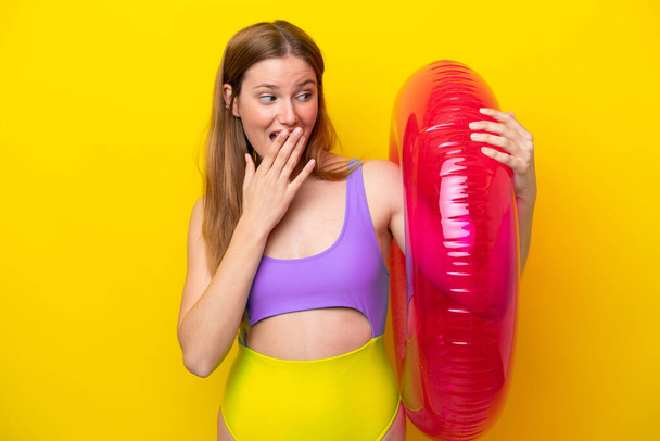 Young caucasian woman holding air mattress isolated on yellow background with surprise and shocked facial expression - Fotó, kép