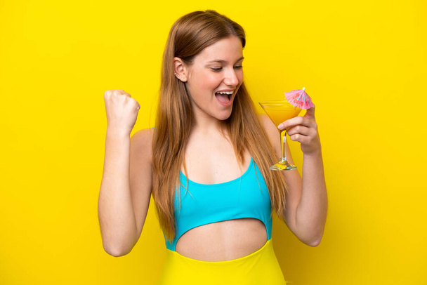 Young caucasian woman holding a cocktail isolated on yellow background celebrating a victory - Foto, afbeelding