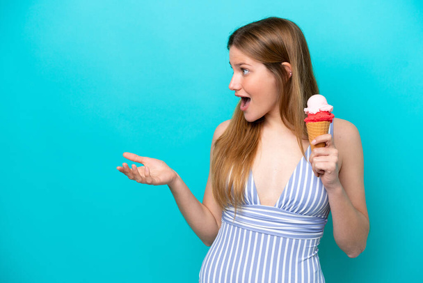 Young caucasian woman in swimsuit eating ice cream isolated on blue background with surprise facial expression - Фото, изображение