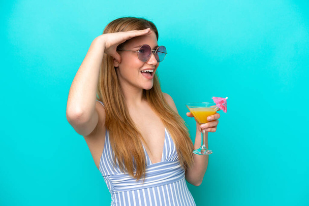 Young woman isolated on blue background in swimsuit and holding a cocktail - Foto, Imagen