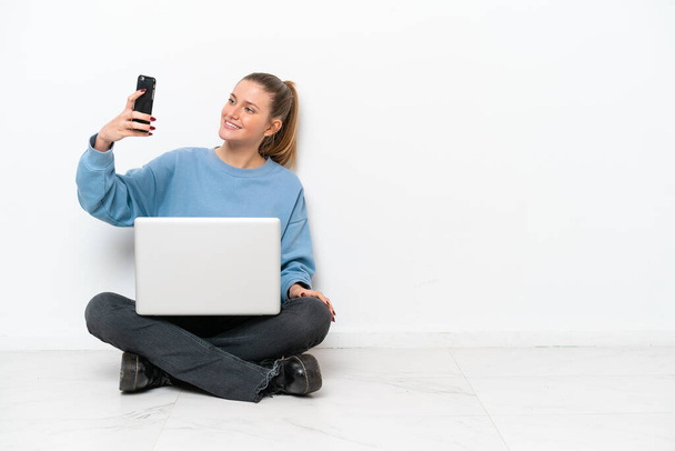 Jeune femme avec un ordinateur portable assis sur le sol faisant un selfie - Photo, image
