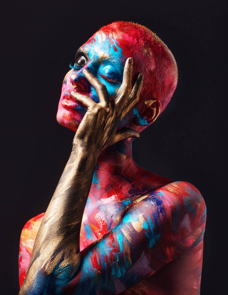 She stood out like never before. Shot of an attractive young woman posing alone in the studio with paint on her face and body. - Photo, Image