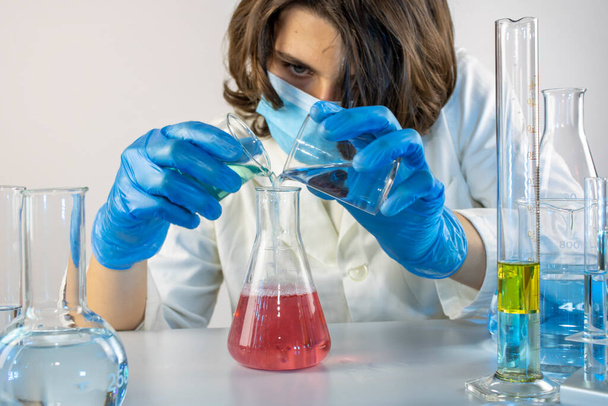 Jeune scientifique mélangeant des liquides avec des béchers et des flacons, en laboratoire - Photo, image