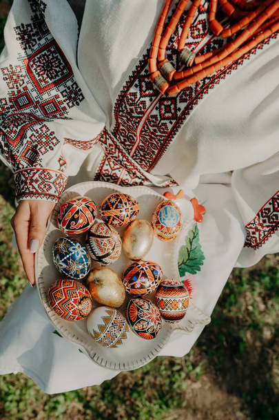 Ukrainian woman holding in hands Easter eggs. Beautiful geometric slavic decoration. Lady in embroidery vyshyvanka dress. - 写真・画像