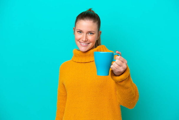 Young caucasian woman holding cup isolated on blue background with happy expression - Photo, image