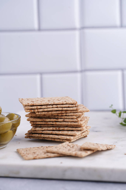Healthy crunchy crisp crackers with sesame seeds and green olives on marble board - 写真・画像