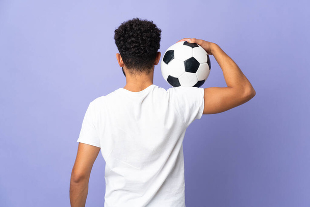 Νεαρός μαροκινός άνδρας απομονωμένος σε μωβ φόντο με μπάλα ποδοσφαίρου - Φωτογραφία, εικόνα